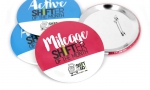 Panachage de badges ronds 88mm.
Visuel : 'Mileage shifter of the month. Logo Shift & Go! accompagné d'un escargot sur skateboard. 
Moins de gaz dans mes voyages / DDD.'